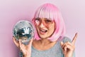 Young caucasian woman wearing pink wig holding disco ball smiling happy pointing with hand and finger to the side Royalty Free Stock Photo