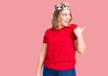 Young caucasian woman wearing princess crown smiling with happy face looking and pointing to the side with thumb up Royalty Free Stock Photo