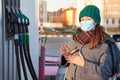 Young woman wearing protective medical mask starting to fuel her car with gasoline at gas station Royalty Free Stock Photo