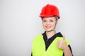 Young caucasian woman wearing red safety hard hat and reflective vest, smiling with thumbs up