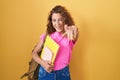 Young caucasian woman wearing student backpack and holding books pointing to you and the camera with fingers, smiling positive and Royalty Free Stock Photo