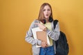 Young caucasian woman wearing student backpack and holding books surprised pointing with finger to the side, open mouth amazed Royalty Free Stock Photo