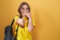 Young caucasian woman wearing student backpack over yellow background laughing at you, pointing finger to the camera with hand Royalty Free Stock Photo