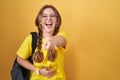 Young caucasian woman wearing student backpack over yellow background laughing at you, pointing finger to the camera with hand Royalty Free Stock Photo