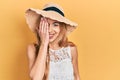Young caucasian woman wearing summer hat covering one eye with hand, confident smile on face and surprise emotion Royalty Free Stock Photo