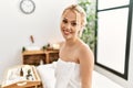 Young caucasian woman wearing towel sitting on massage board at beauty salon