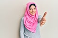 Young caucasian woman wearing traditional islamic hijab scarf smiling friendly offering handshake as greeting and welcoming Royalty Free Stock Photo