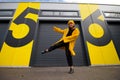 Caucasian woman wearing a yellow hat and a yellow raincoat dancing on a city street, positive active lifestyle and street
