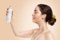 A young Caucasian woman, with wet skin, holding a bottle of cosmetics. Copy space. Side view. Beige background. Concept of