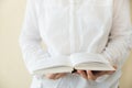 Young caucasian woman in white cotton shirt stands holds open book in hands. Emptry wall background. College school university