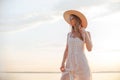 Young caucasian woman in white dress, summer hat and sunglasses posing on beach on sunset Royalty Free Stock Photo