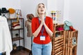 Young caucasian woman working as manager at retail boutique begging and praying with hands together with hope expression on face