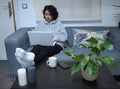 Young caucasian woman working on her laptop with her feet on the table, in pajamas, sitting on the sofa with a cup of coffee Royalty Free Stock Photo