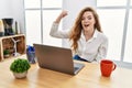 Young caucasian woman working at the office using computer laptop angry and mad raising fist frustrated and furious while shouting Royalty Free Stock Photo