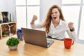 Young caucasian woman working at the office using computer laptop angry and mad raising fists frustrated and furious while Royalty Free Stock Photo