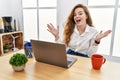 Young caucasian woman working at the office using computer laptop celebrating crazy and amazed for success with arms raised and Royalty Free Stock Photo