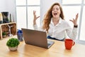 Young caucasian woman working at the office using computer laptop celebrating mad and crazy for success with arms raised and Royalty Free Stock Photo
