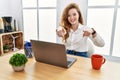 Young caucasian woman working at the office using computer laptop pointing to you and the camera with fingers, smiling positive Royalty Free Stock Photo