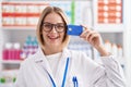 Young caucasian woman working at pharmacy drugstore holding credit card looking positive and happy standing and smiling with a Royalty Free Stock Photo