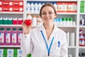 Young caucasian woman working at pharmacy drugstore holding red heart looking positive and happy standing and smiling with a Royalty Free Stock Photo