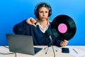 Young caucasian woman working at radio studio holding vinyl disc with angry face, negative sign showing dislike with thumbs down, Royalty Free Stock Photo