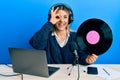 Young caucasian woman working at radio studio holding vinyl disc smiling happy doing ok sign with hand on eye looking through Royalty Free Stock Photo