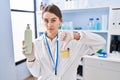 Young caucasian woman working at scientist laboratory holding body lotion with angry face, negative sign showing dislike with