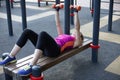 Young caucasian woman workouts on the park sports ground with dumbbells, laying on the sport bar; black and lilac sportswear, prot Royalty Free Stock Photo