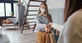 Young Caucasian woman wearing mask opens apartment door to get delivery bags from courier on self isolation lockdown.