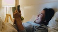 Young cell phone addict Asian lady using tablet checking social media feeling happy smiling while lying on bed before she sleeping Royalty Free Stock Photo