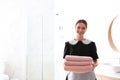 Young chambermaid holding stack of fresh towels in bathroom. Space for text