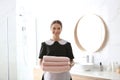 Young chambermaid holding stack of fresh towels in bathroom