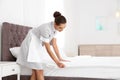 Young chambermaid making bed