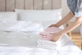 Young chambermaid putting stack of fresh towels on bed in hotel room. Space for text Royalty Free Stock Photo