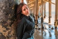 A young charming brunette woman in a black shirt and denim shorts poses under a pier on the beach of Malibu, California Royalty Free Stock Photo