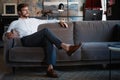 Young and charming businessman is thinking about business while sitting on the sofa in his modern office.