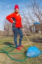 Young charming female gardener stands in her garden on blue sky background, closeup garden tools, vertical picture
