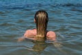 Young charming girl bathes in the sea and dries her hair in the water, rear view Royalty Free Stock Photo