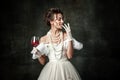 Young charming girl in image of medieval renaissance person or viscountess tasting wine isolated on dark vintage