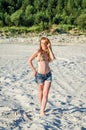 Young charming girl in short denim shorts and bikini swimsuit with long hair walking along the sand quarry sand extractive Royalty Free Stock Photo