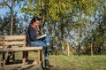 Young charming girl student sits on a bench in the autumn forest and reads a book Royalty Free Stock Photo