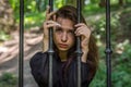 Young charming girl the teenager with long hair sitting behind bars in prison prisoner in a medieval jail with sad, pleading eyes Royalty Free Stock Photo