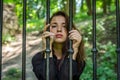 Young charming girl the teenager with long hair sitting behind bars in prison prisoner in a medieval jail with sad, pleading eyes Royalty Free Stock Photo