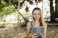 Young charming girl using tablet and riding swing on sand, wearing jeans sundress. Royalty Free Stock Photo