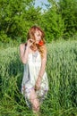 Young charming girl in a white sundress beautiful, walking in the field among the wheat spikelets with flower red poppies in Royalty Free Stock Photo