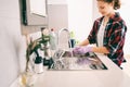 Young charming happy smiling girl woman washing dishes in gloves in the kitchen. House Hygiene and Cleaning Service Concept Royalty Free Stock Photo