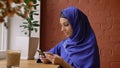 Young charming muslim woman in hijab rewrite info from card to her phone and smiling, sitting in cafe, beautiful female