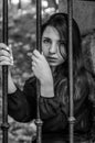 Young charming teenager girl with long dark hair sitting behind bars in a prison in the old castle fortress serving a sentence for Royalty Free Stock Photo