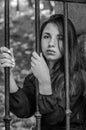 Young charming teenager girl with long dark hair sitting behind bars in a prison in the old castle fortress serving a sentence for Royalty Free Stock Photo