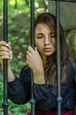 Young charming teenager girl with long dark hair sitting behind bars in a prison in the old castle fortress serving a sentence for Royalty Free Stock Photo